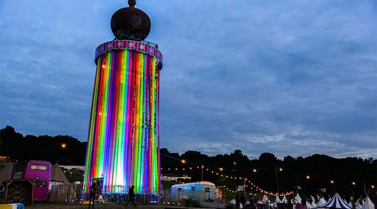 Une tour éclairée dotée de rayures multicolores au crépuscule avec des tentes sur le côté