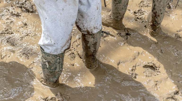 Benen van twee mensen met regenlaarzen die in de modder staan