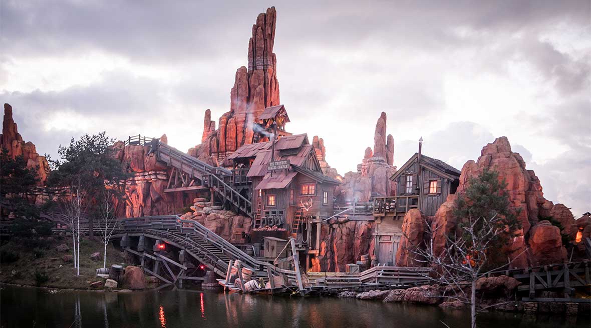 Exterior of the Big Thunder Mountain Ride in Disneyland Paris with wooden rollercoaster tracks and mountains in the background