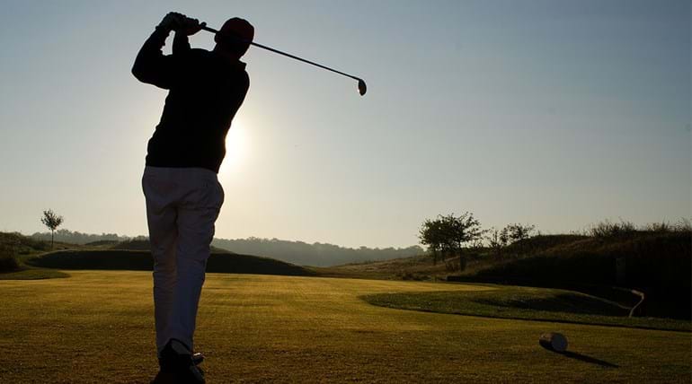 Man speelt golf op glooiende baan in avondlicht