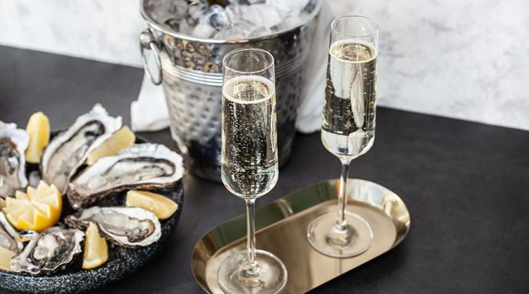 Oysters in shells on a plate, an ice bucket of champagne and two glasses of champagne