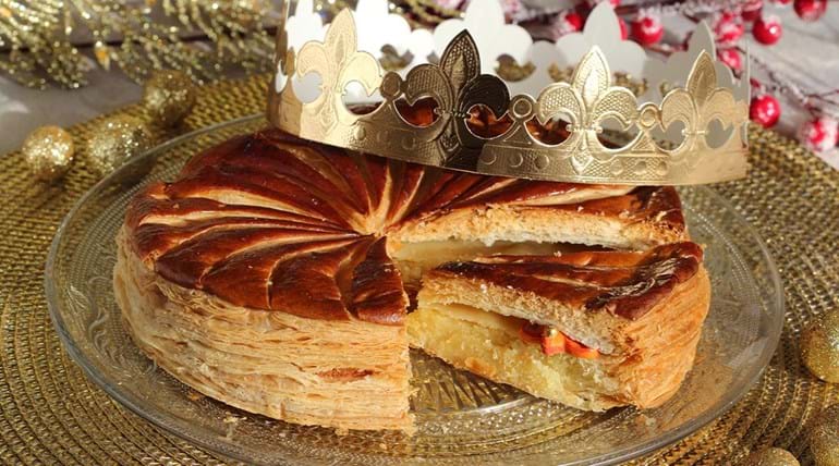 A puff pastry tart with a cardboard crown on top of it and seasonal decorations littered around the plate 