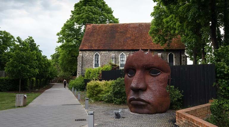 Metershoog metalen gezichtsmasker naast een oud gebouw in Canterbury