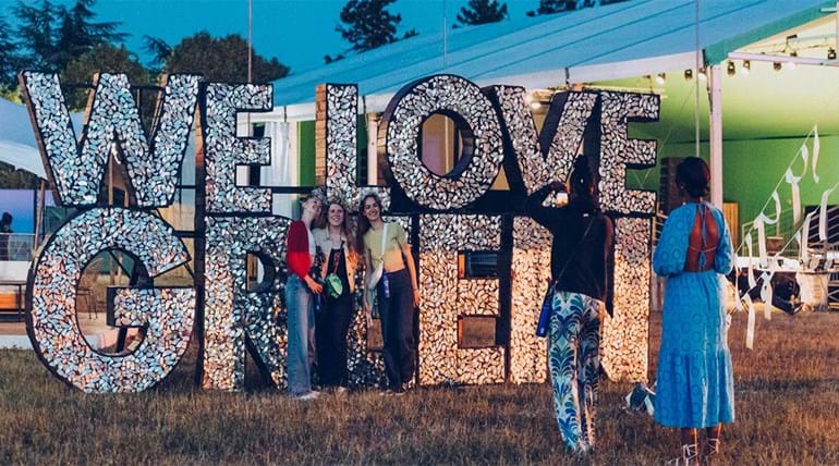 A group of festival goers being photographed in front of a festival’s sign