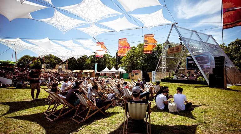 Festival goers sit in deckchairs in front of a small stage where a panel discussion is being held 