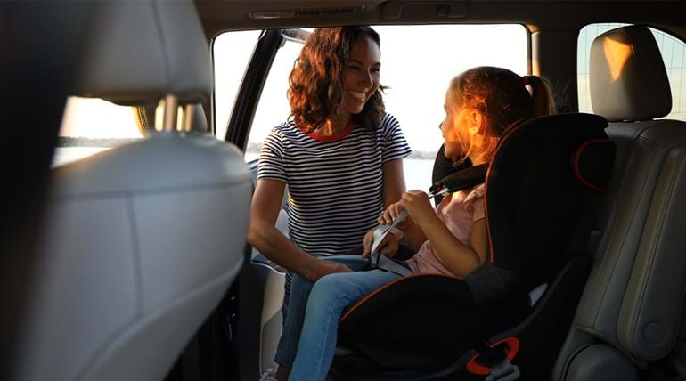 woman placing seatbelt on child in the back of a car