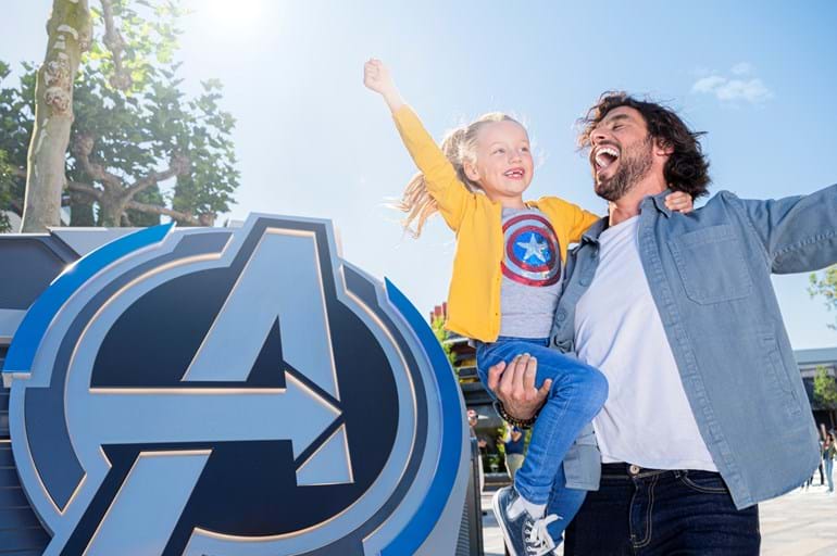 A happy young girl in a Captain America t-shirt being held by a happy parent at a theme park