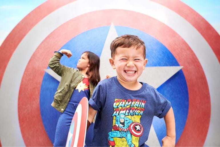 A very excited little boy in a Captain America T-shirt with a little girl in the background striking a super hero pose 