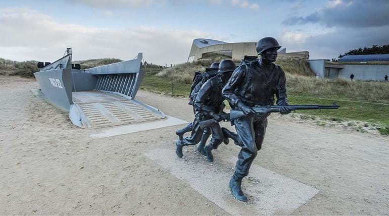 Statues of soldiers charging from a landing craft. Artwork memorial on a beach
