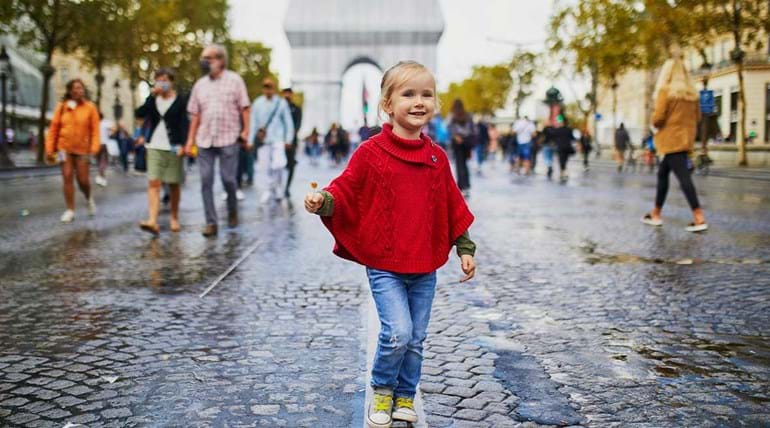 Smiling young girl walking down a wide cobbled city street with other pedestrians