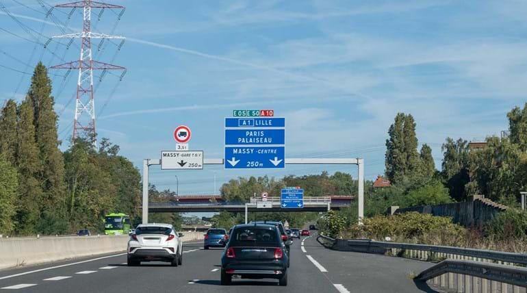 A motorway in France with cars driving and a vertically mounted road sign above the carriageway