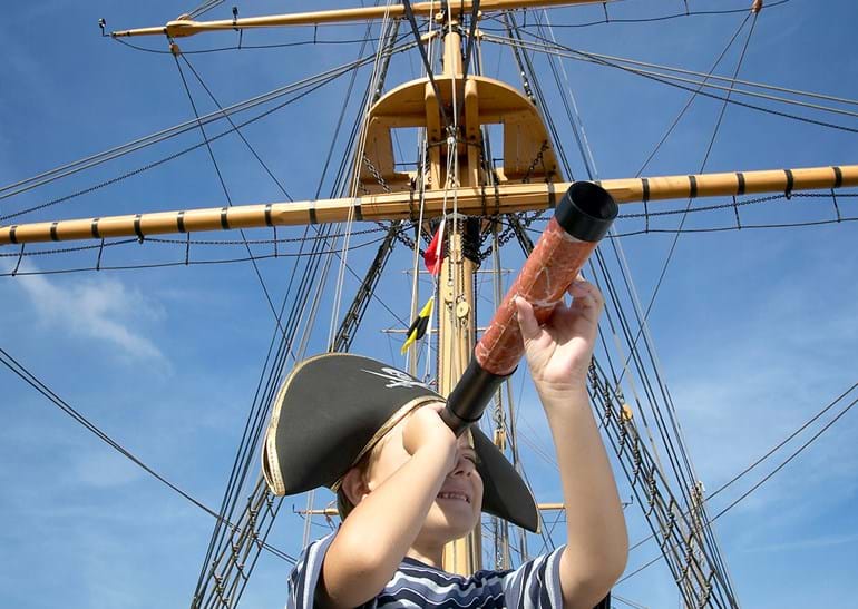 Un enfant équipé d’un chapeau de pirate et d’une longue vue devant un grand mât