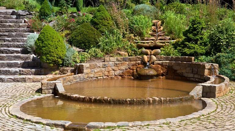 Des bassins, sculptures et escalier en pierre dans un jardin verdoyant