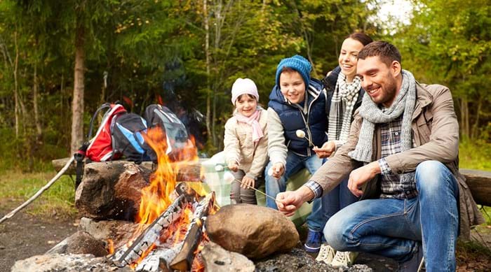 Familie rond een kampvuur in bosrijke omgeving op een camping die gezellig samen marshmallows roosteren in Engeland